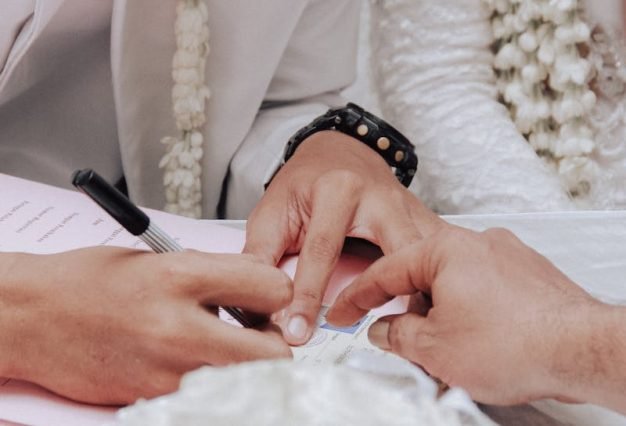 Photo by Arif Syuhada Close-up of a groom and bride signing their wedding contract during a ceremony.